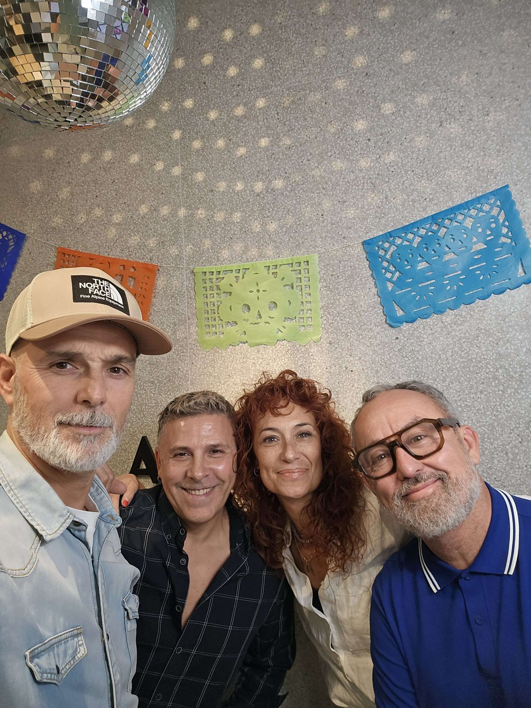 El equipo de Alvado 3, sonriendo junto al rótulo del salón con papel picado y la bola de espejos